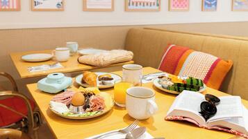 Une table mise pour le petit-déjeuner, avec des assiettes remplies de nourriture, une tasse de café, un livre et une paire de lunettes de soleil.