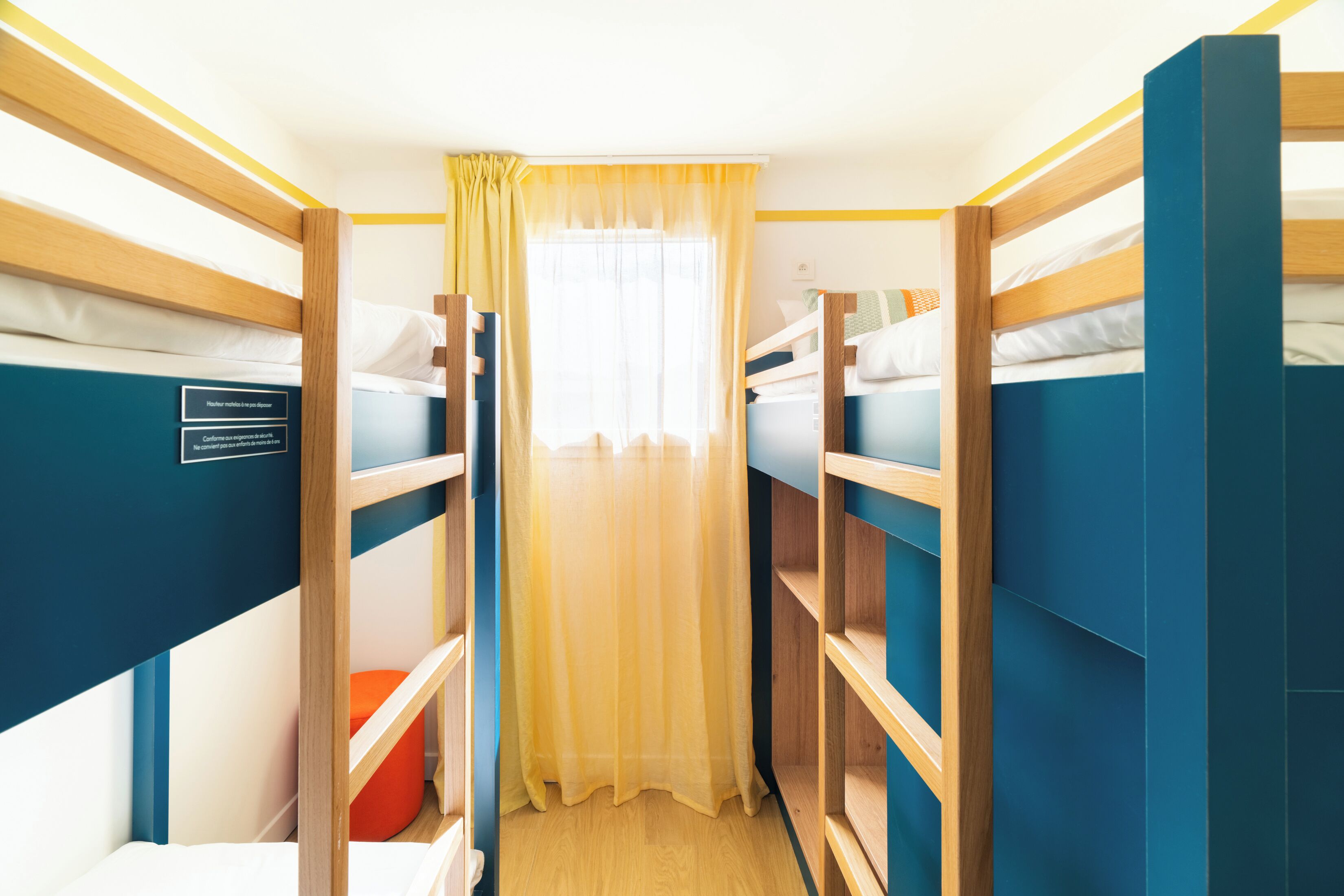 A bunk bed room with a curtain, a small orange stool, and a sign on the wall.
