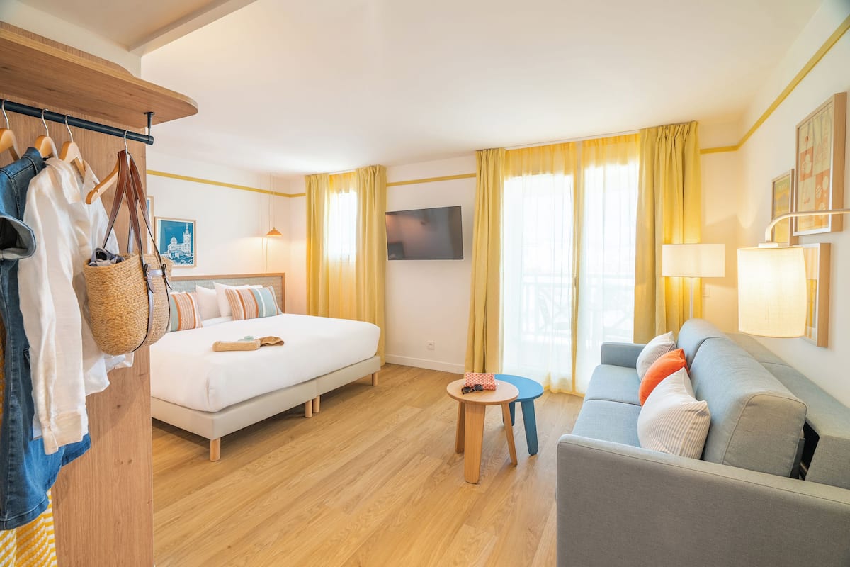 A hotel room with a bed, a sofa, a TV, and a wooden wardrobe.