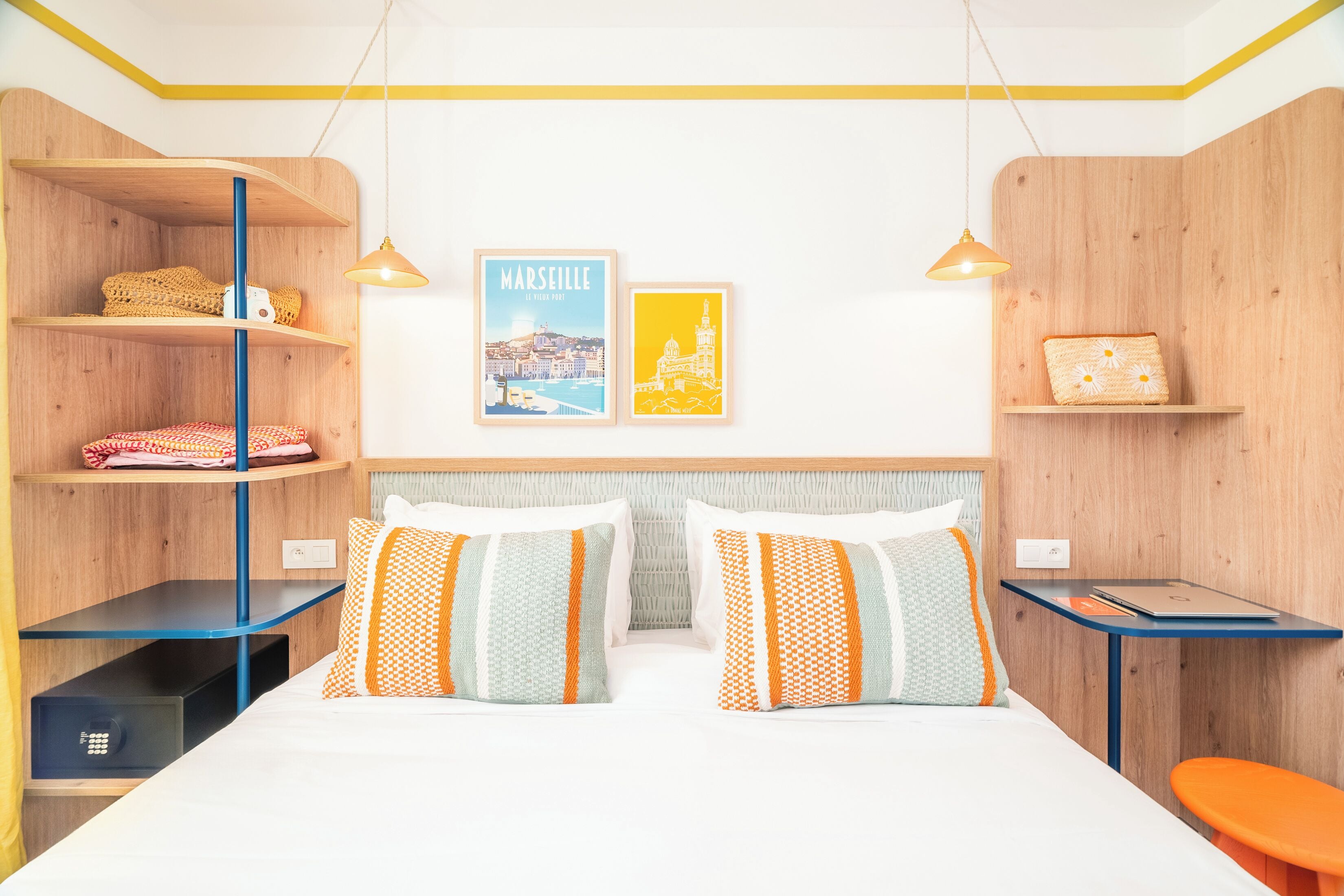 Una habitación de hotel moderna con una cama, dos almohadas, una mesita de noche, un escritorio, una silla y dos cuadros en la pared.