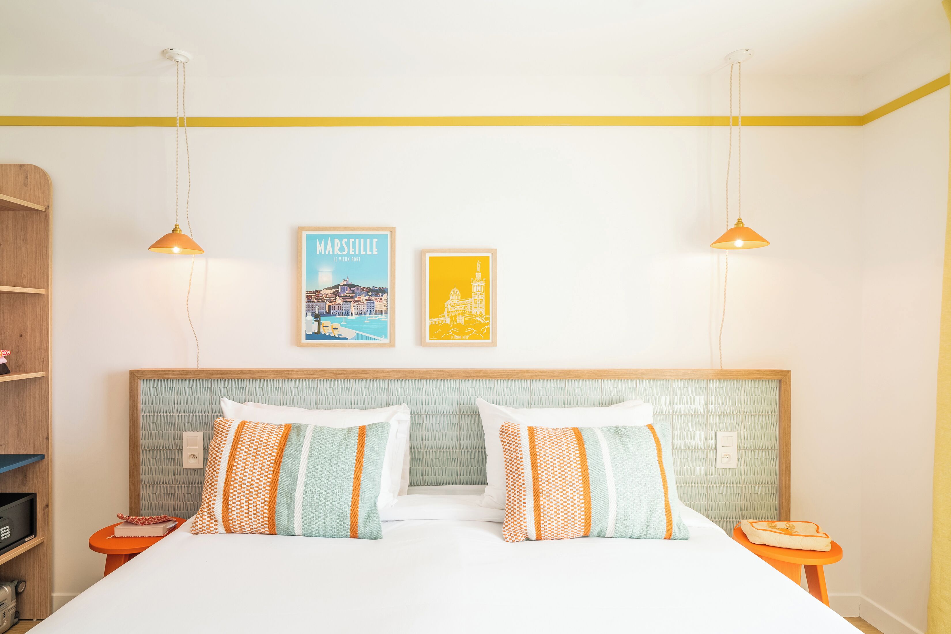 Quarto de hotel com cama, duas mesas de cabeceira, uma estante e dois quadros na parede.