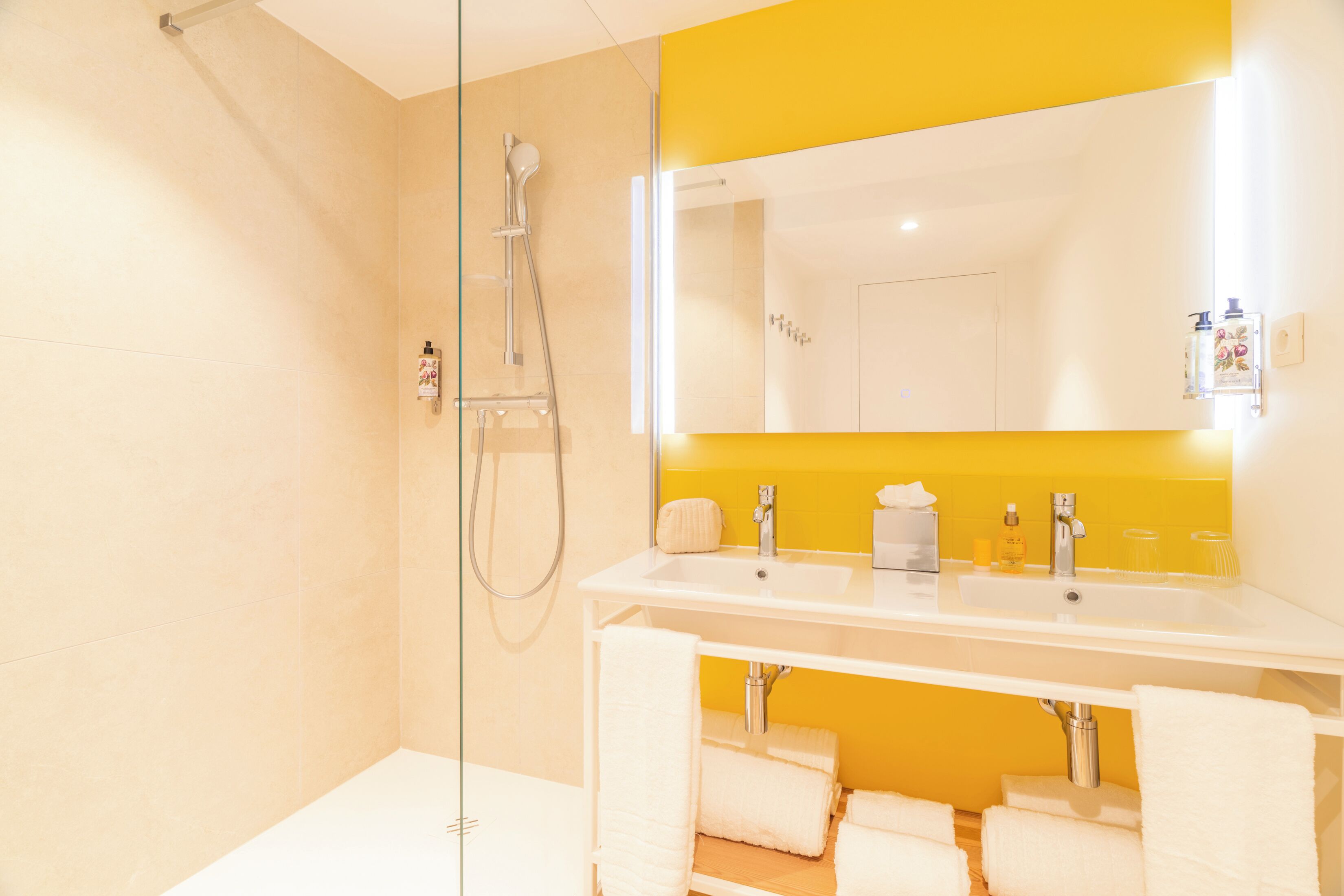A bathroom with a glass shower enclosure, a white sink, and a mirror with a yellow accent wall.