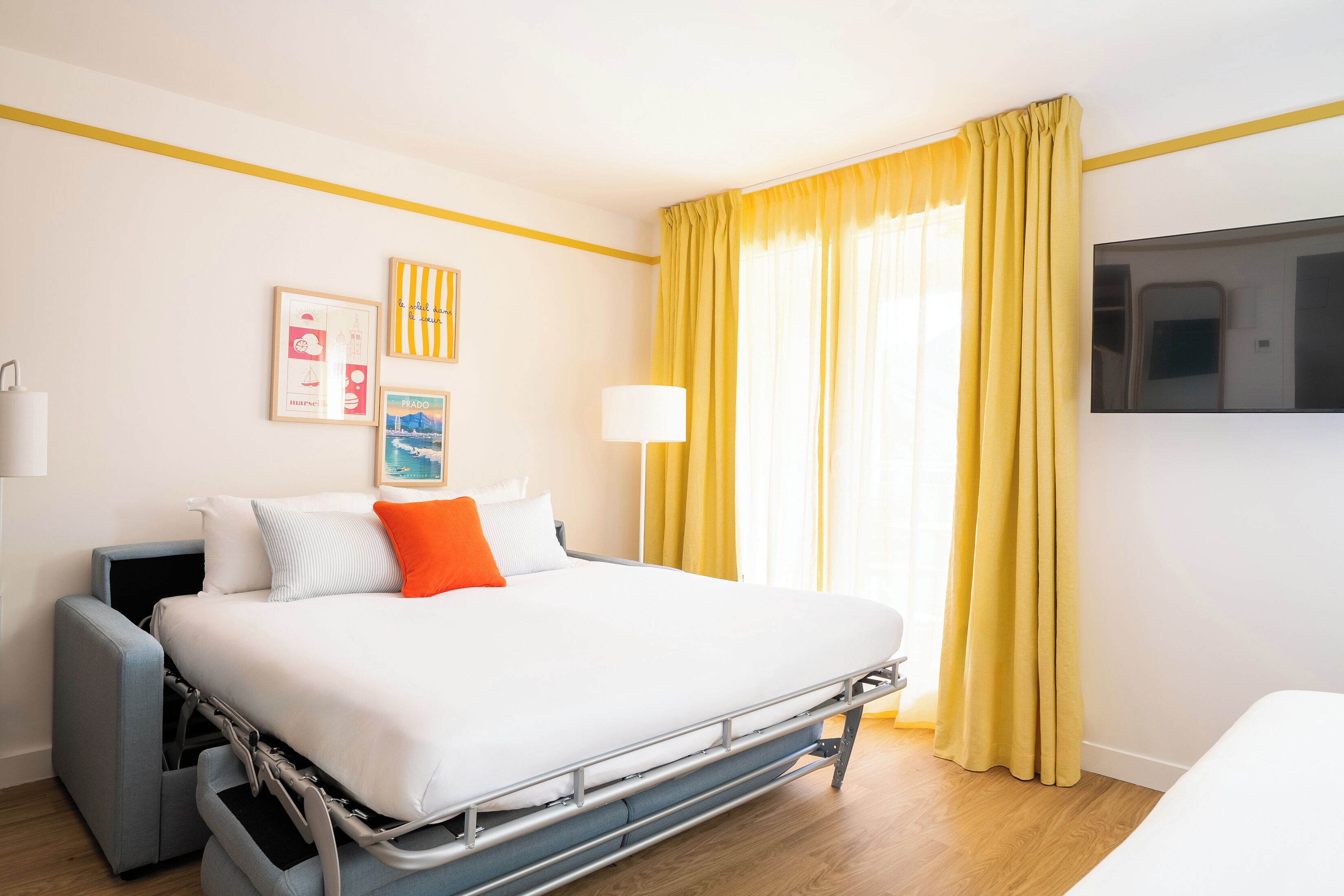 Habitación de hotel con cama, televisor, escritorio y ventana con cortinas.