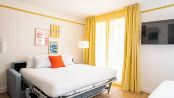 Habitación de hotel con cama, televisor, escritorio y ventana con cortinas.