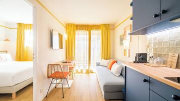 A compact hotel room with a bed, a sofa, a dining area, and a kitchenette.