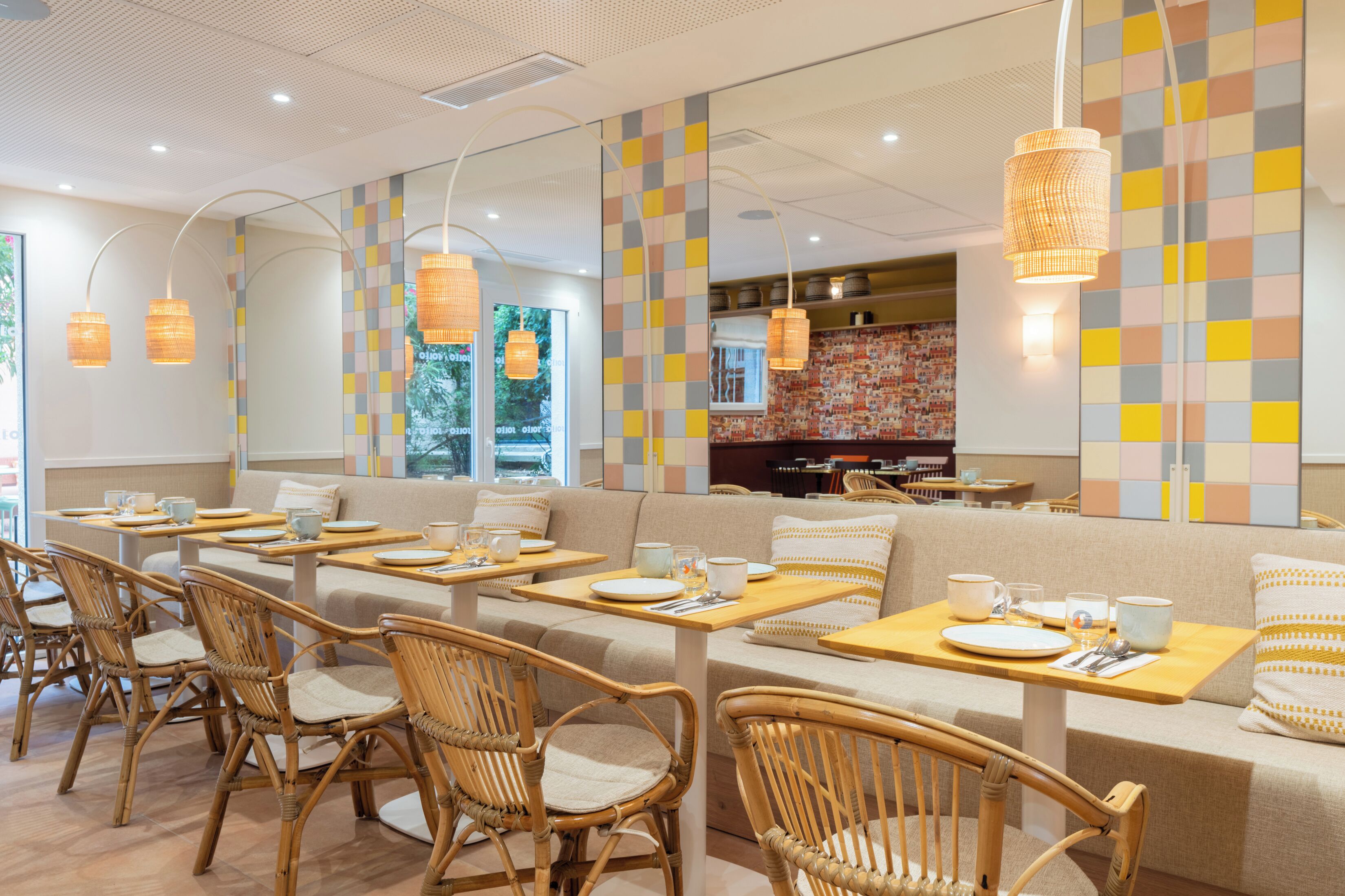 Un restaurante con mobiliario de madera, una pared colorida y lámparas colgantes.