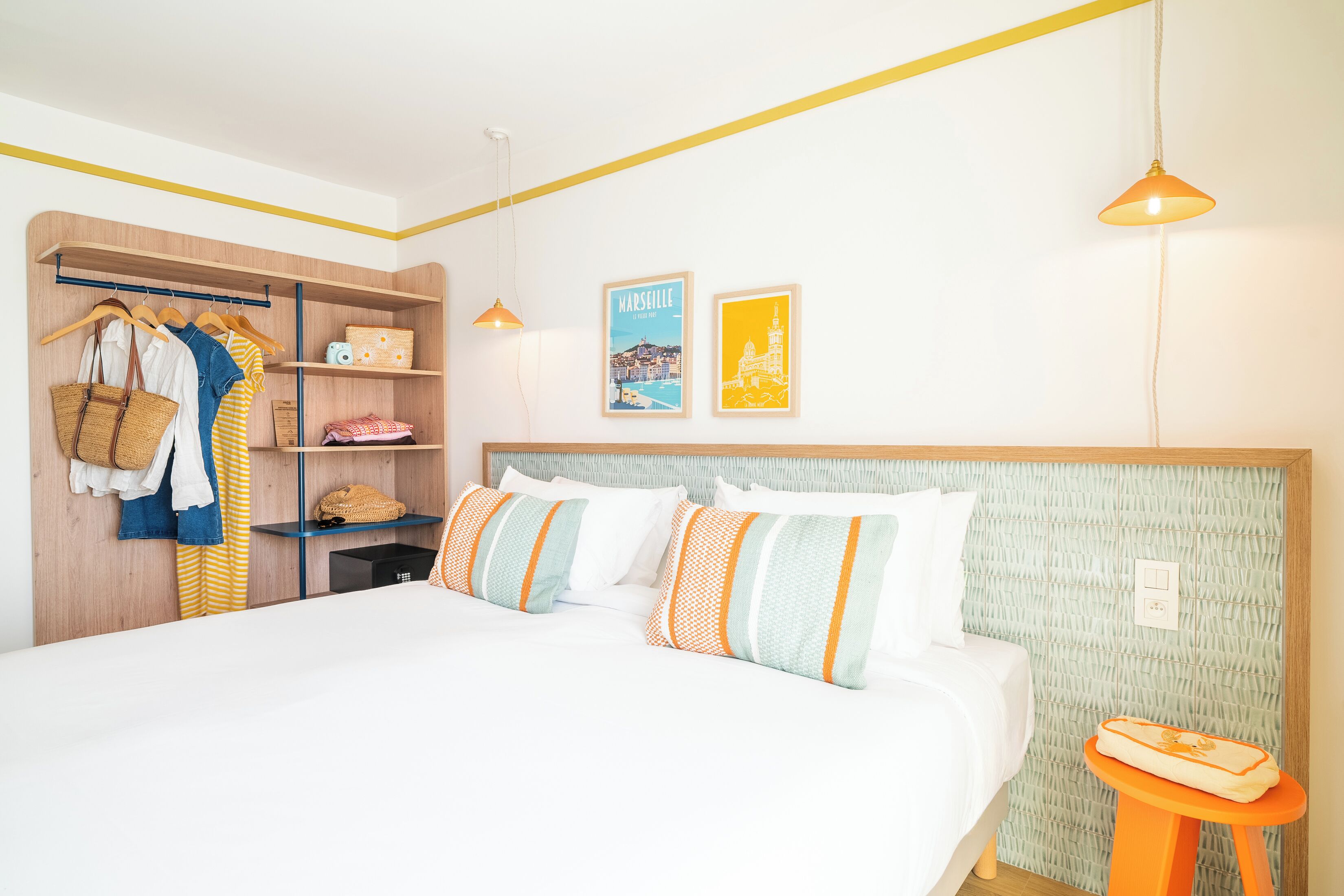 Un dormitorio con cama, armario, cesta colgante, una mesita y dos cuadros en la pared.