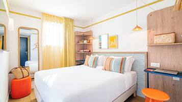 Una camera d'albergo ordinata con un letto grande, una testiera in legno, una scrivania piccola e uno sgabello.