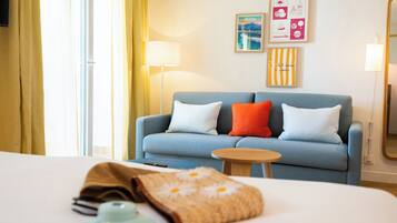 A hotel room with a bed, a blue sofa with pillows, a small wooden side table, and a lamp.