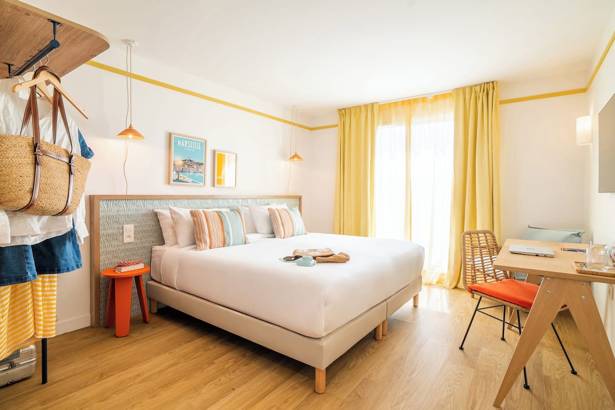 A bedroom with a bed, a desk, a chair, a hanging basket, and a small stool.