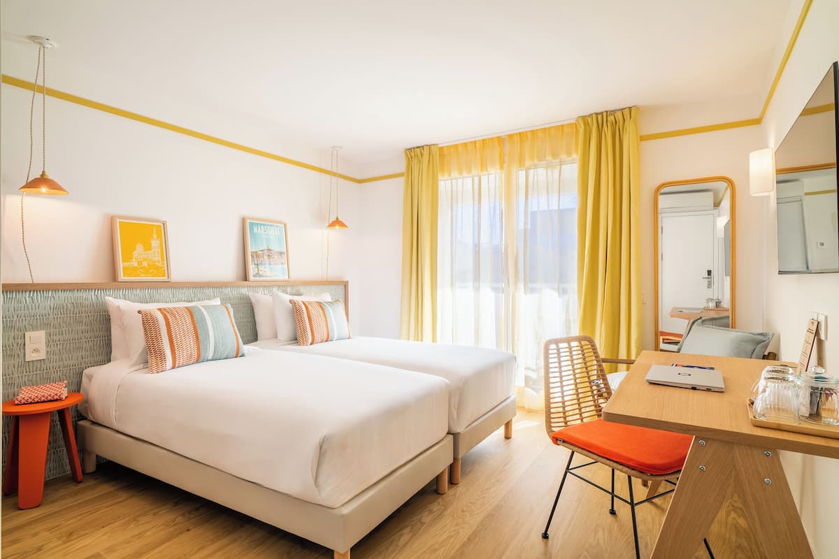 A hotel room with a bed, a desk with a laptop, a chair, and a mirror.