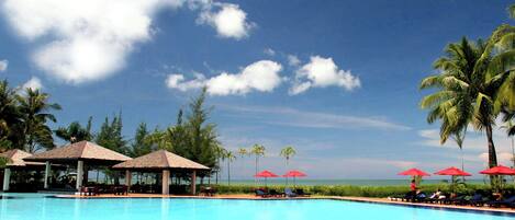 A swimming pool with lounge chairs and umbrellas, surrounded by palm trees and a view of the ocean.