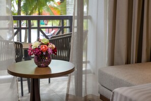 Une chambre d’hôtel avec un lit, une table ronde ornée d’un vase de fleurs et un balcon avec des chaises.