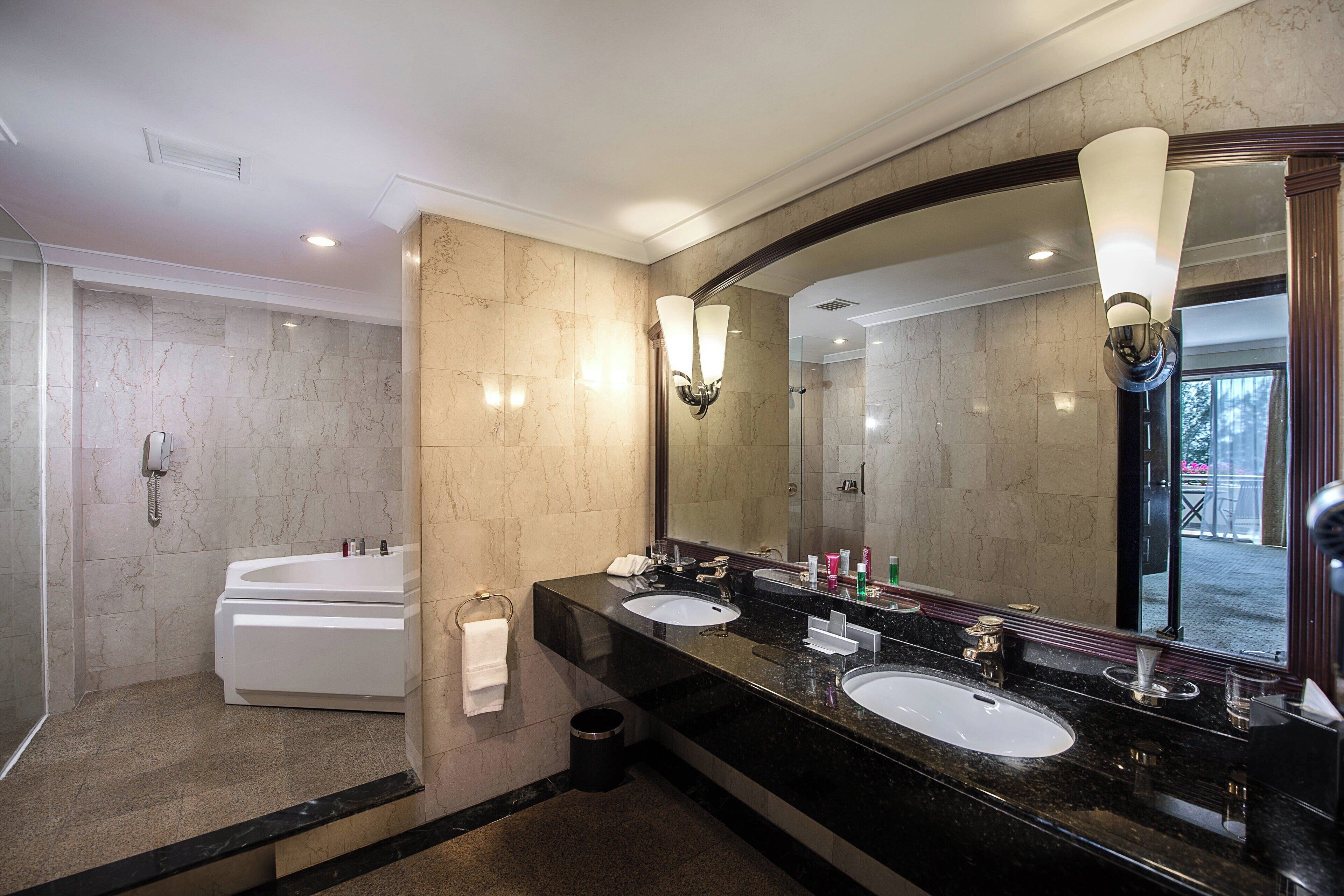 Un baño moderno con un espejo grande, dos lavamanos, una bañera y una ducha.