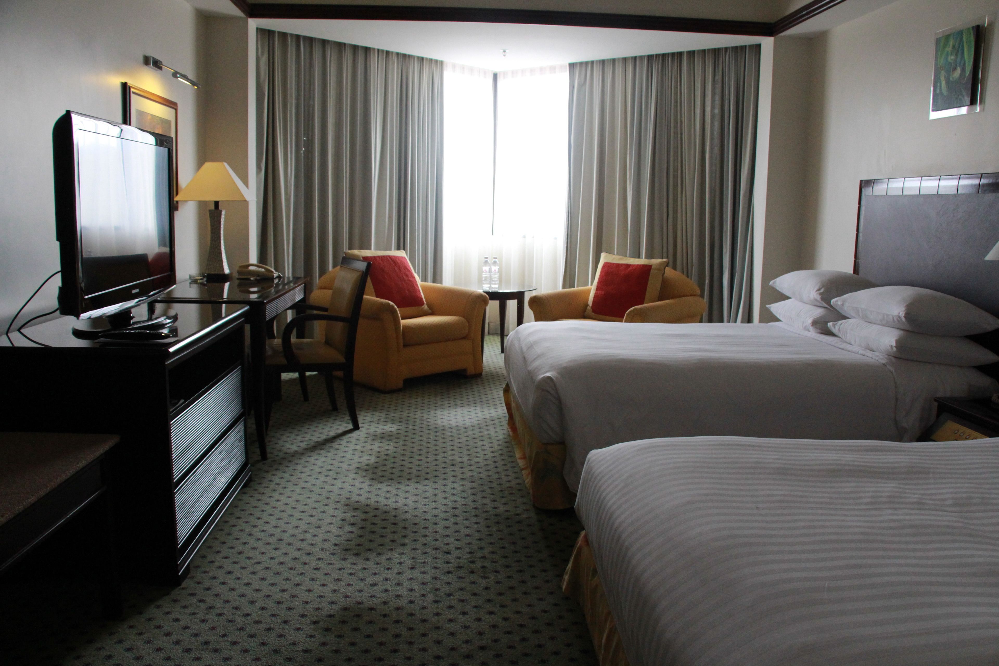 A hotel room with two beds, a desk with a television, a chair, and a lamp.