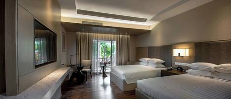 A hotel room with a large bed, a smaller bed, a TV mounted on the wall, a desk with a chair, and a window with curtains.