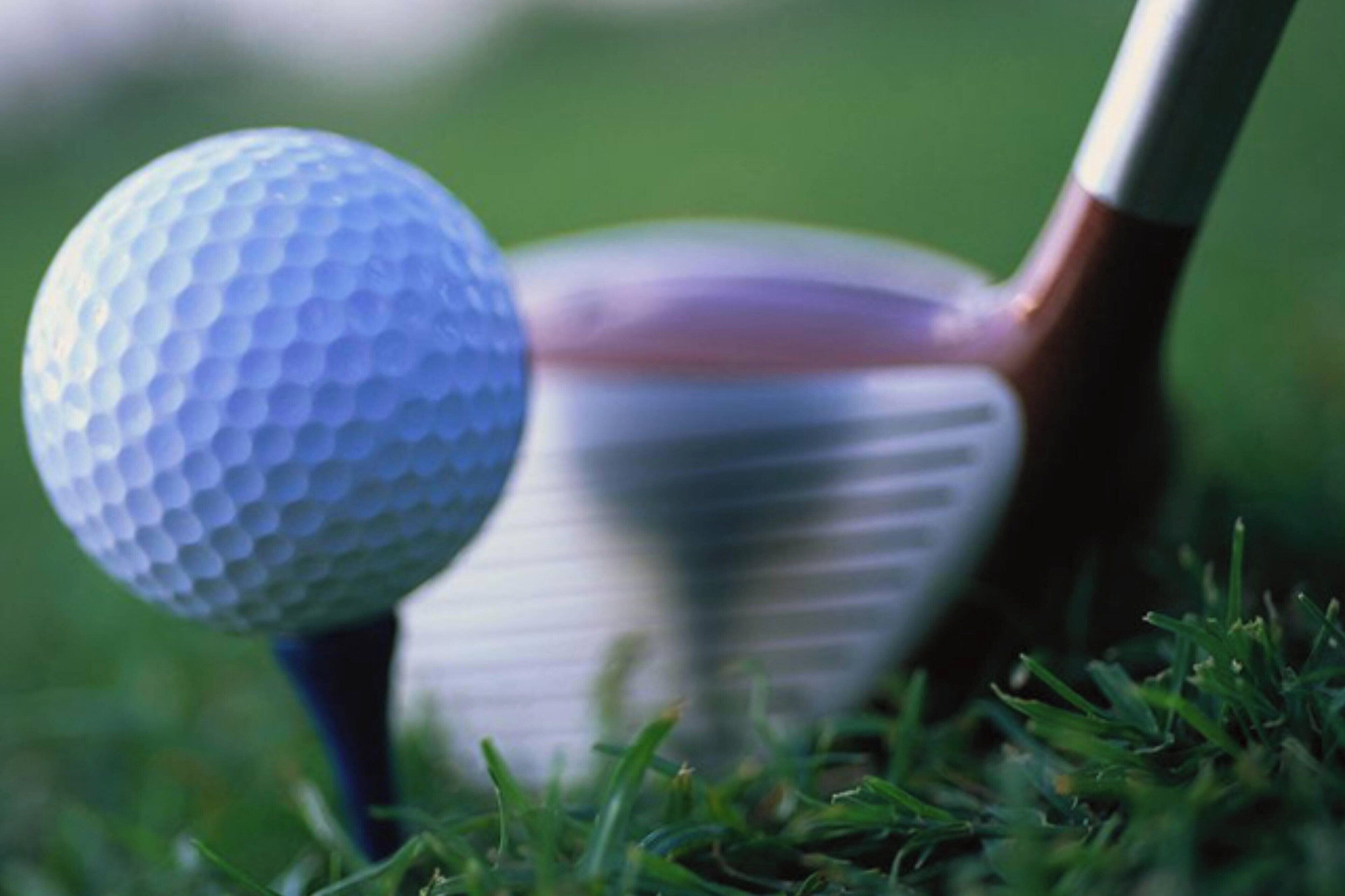 A golf ball on a tee with a golf club in the background.