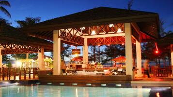 A poolside bar area with a covered seating area and a pool.