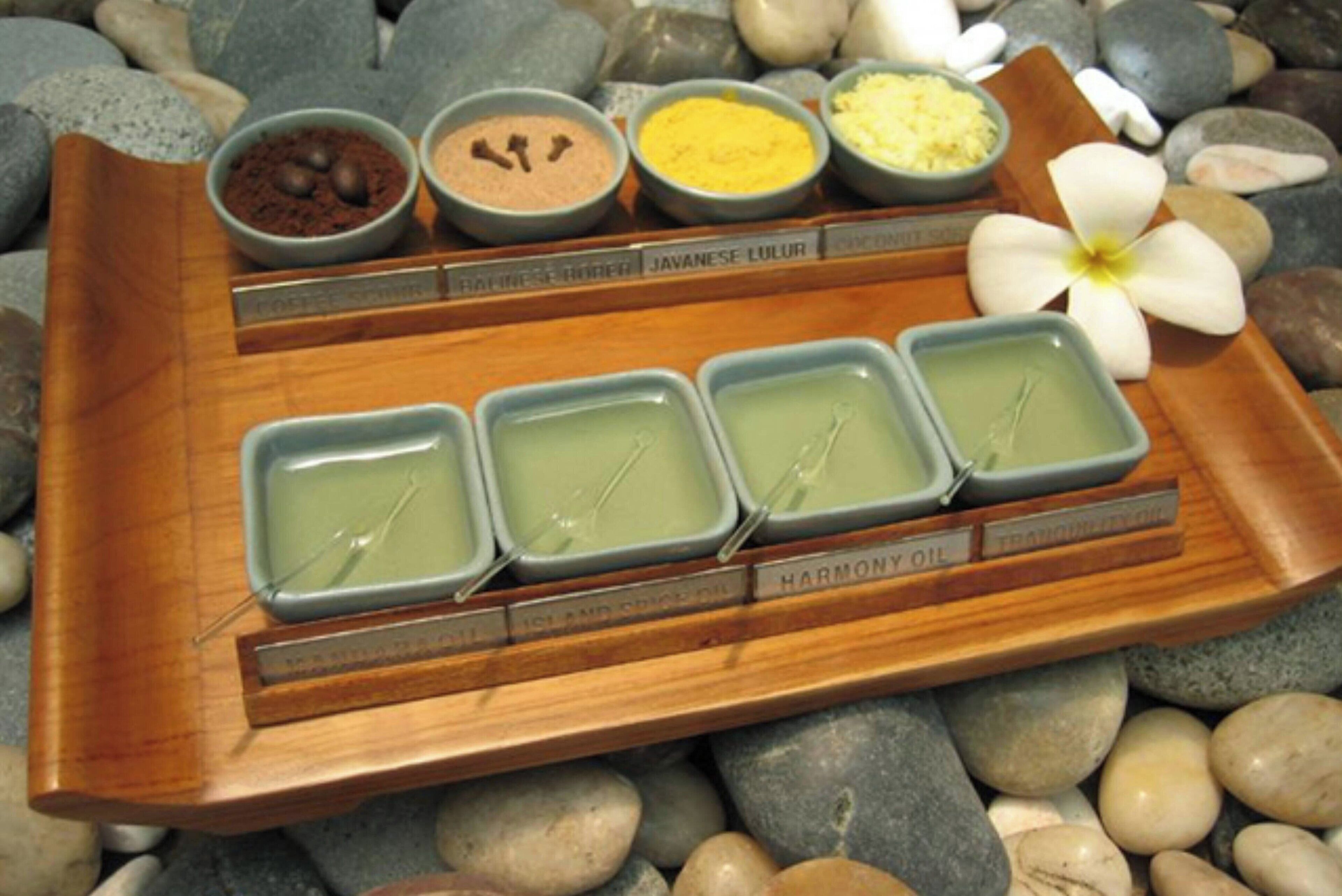 Una bandeja de madera con recipientes etiquetados de varios aceites y polvos, sobre un lecho de piedras lisas.