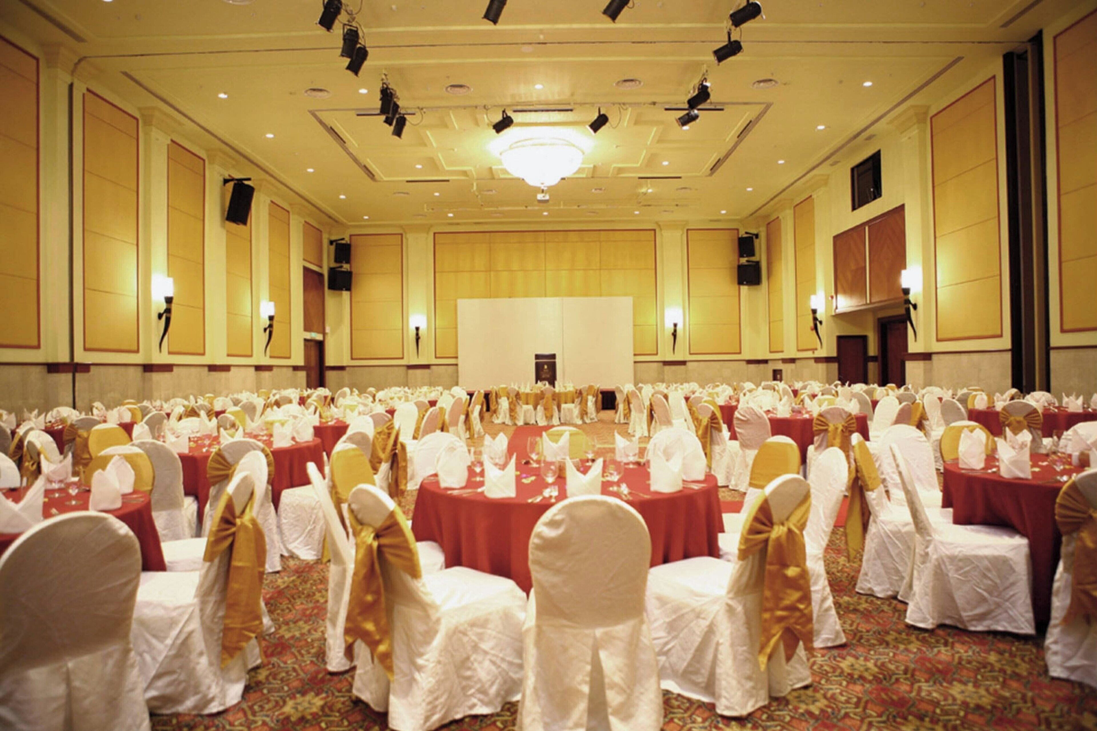 A large banquet hall with rows of tables and chairs, a stage, and a chandelier.