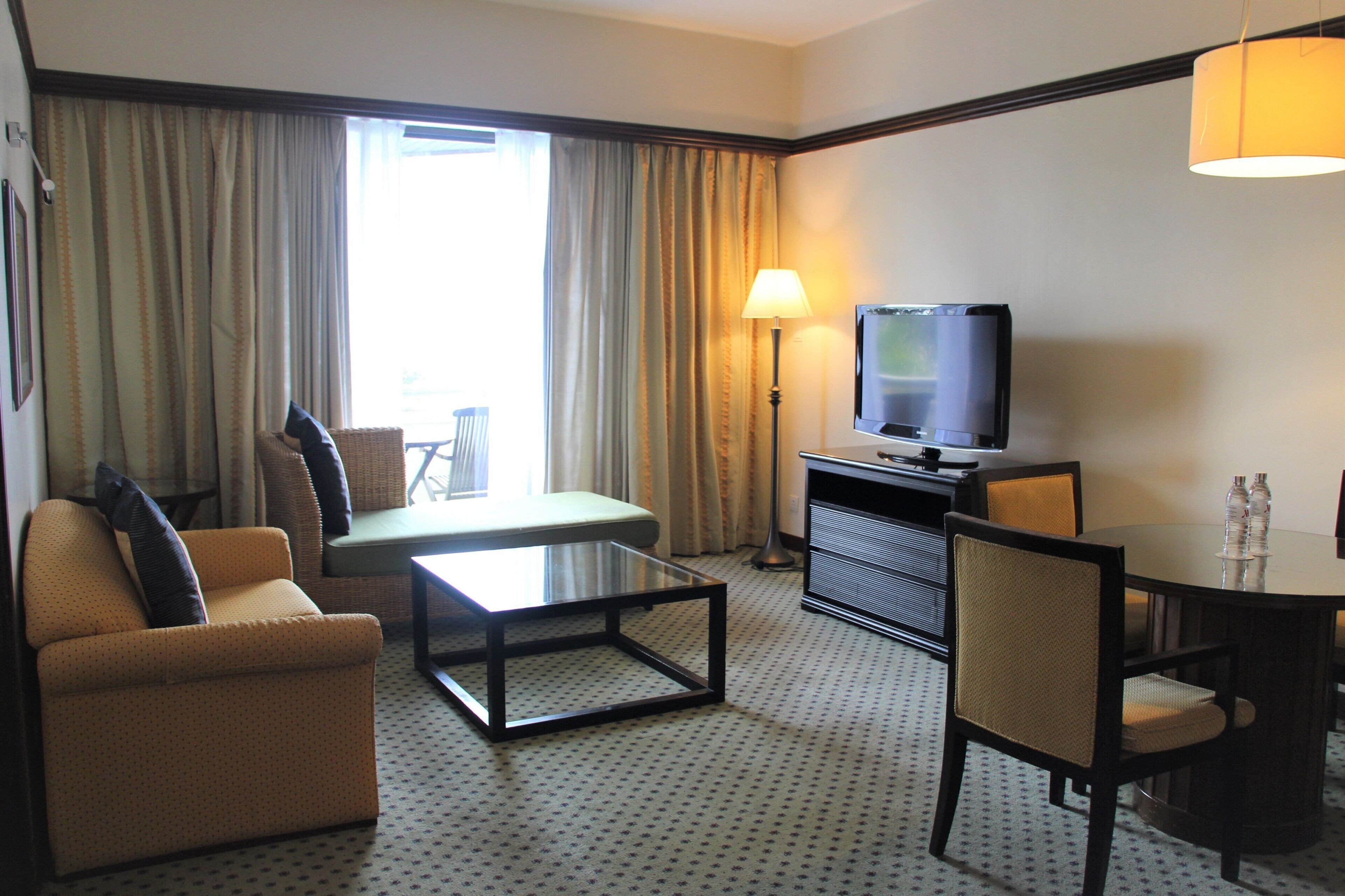 Habitación de hotel con sofá, una pequeña mesa, televisor, lámpara y una mesa de comedor con sillas.