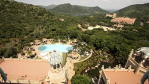 A resort with a large pool, palm trees, and a view of the mountains. - The Palace of the Lost City at Sun City Resort (Moses Kotane)