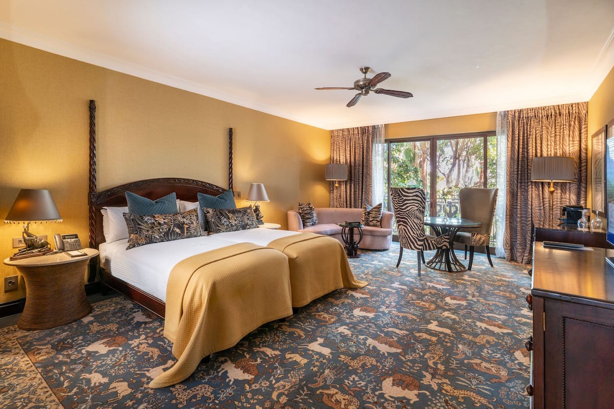 A hotel room with a large bed, a sofa, a dining table, and a zebra-patterned chair.