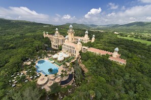 A large, historic building with multiple towers and domes, surrounded by lush greenery and a swimming pool.