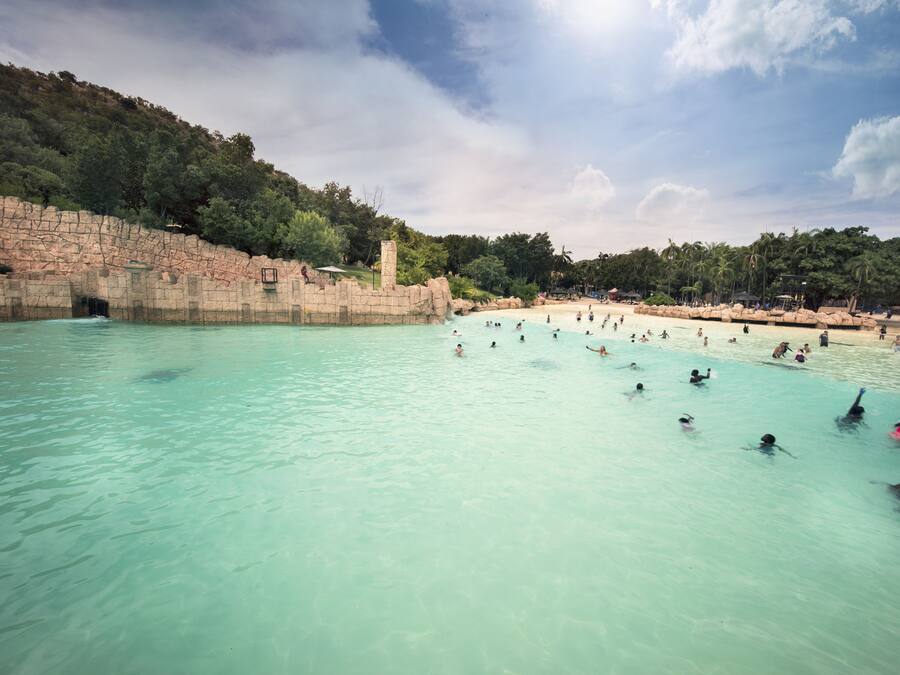 Une grande piscine extérieure entourée d’une falaise rocheuse et d’arbres.