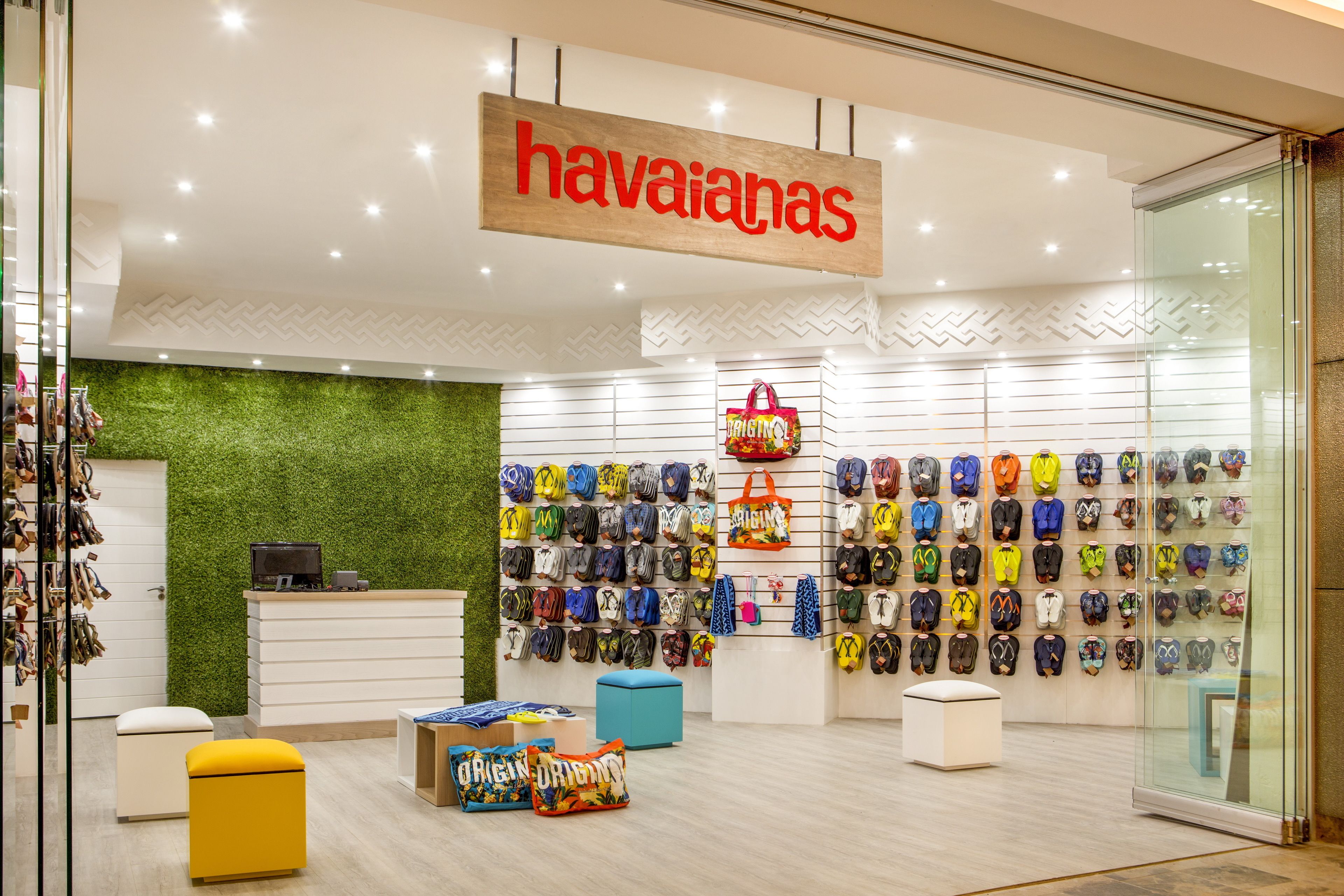 L’intérieur d’un magasin avec un mur vert, une enseigne en bois sur laquelle on peut lire « Havaianas », et des étagères remplies de sacs et de chaussures colorés.