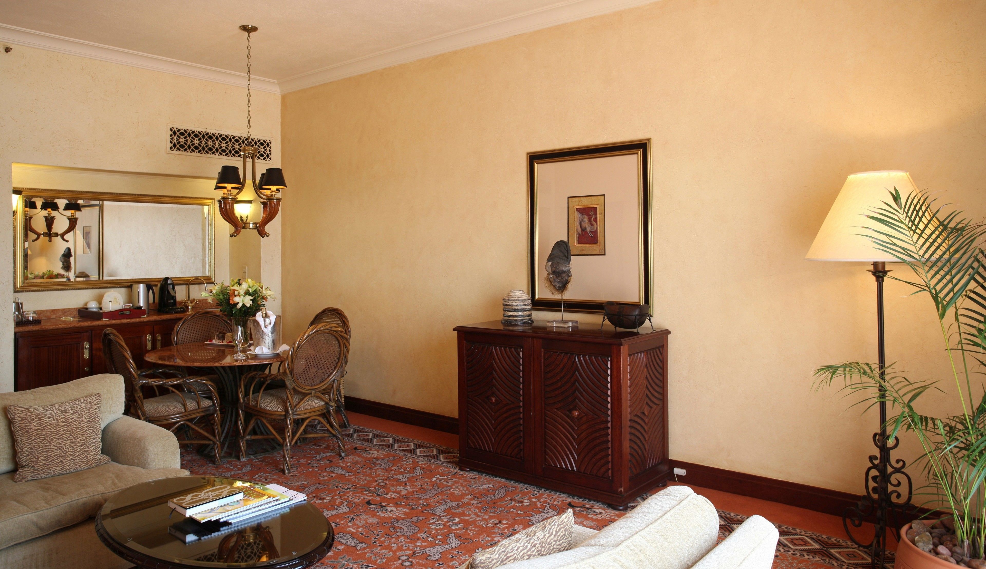A living room with a sofa, a coffee table, a dining area with a table and chairs, a decorative cabinet, a lamp, and a large mirror.