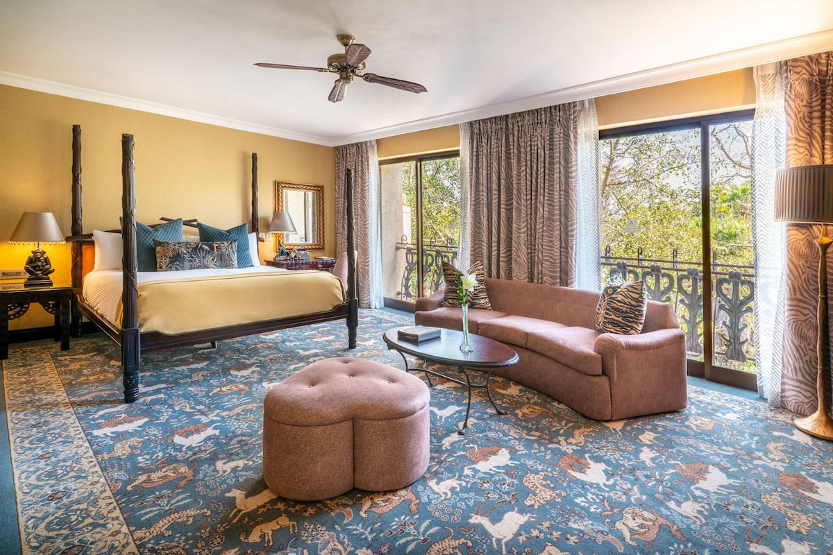 A hotel room with a four-poster bed, a sofa, a coffee table, and a decorative ottoman.