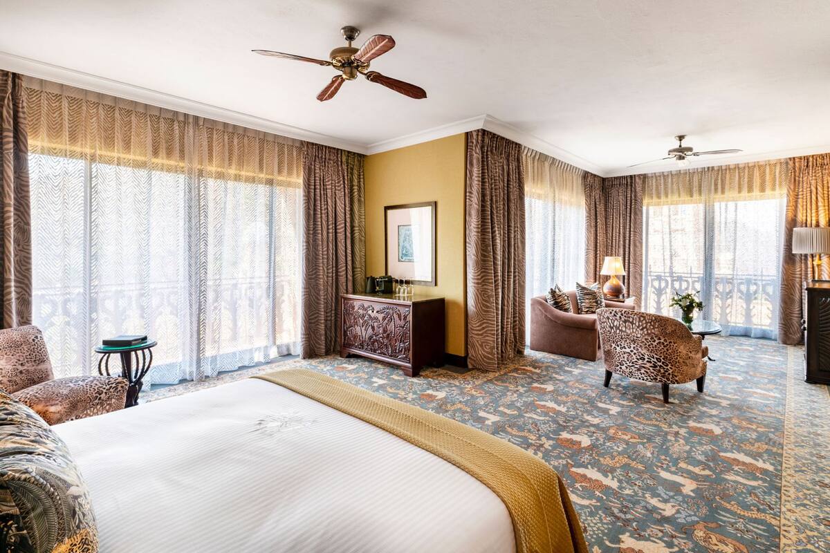 A hotel room with a large bed, a desk, a chair, and a balcony with a view.