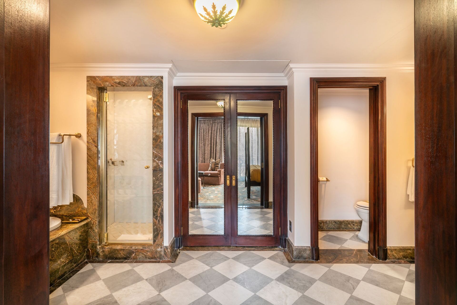 A hotel lobby with a checkered floor, a marble wall, and a wooden door leading to a bedroom.