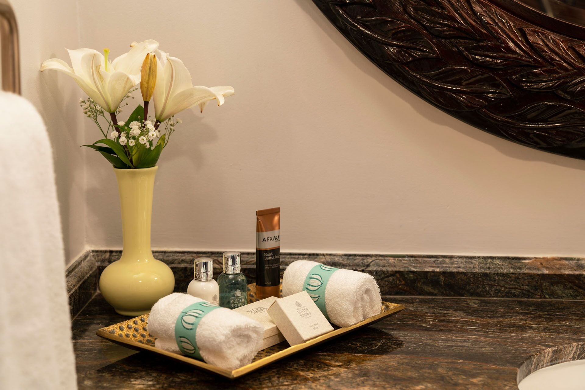 Un tocador de baño con artículos de aseo, un jarrón de flores y un adorno de pared.