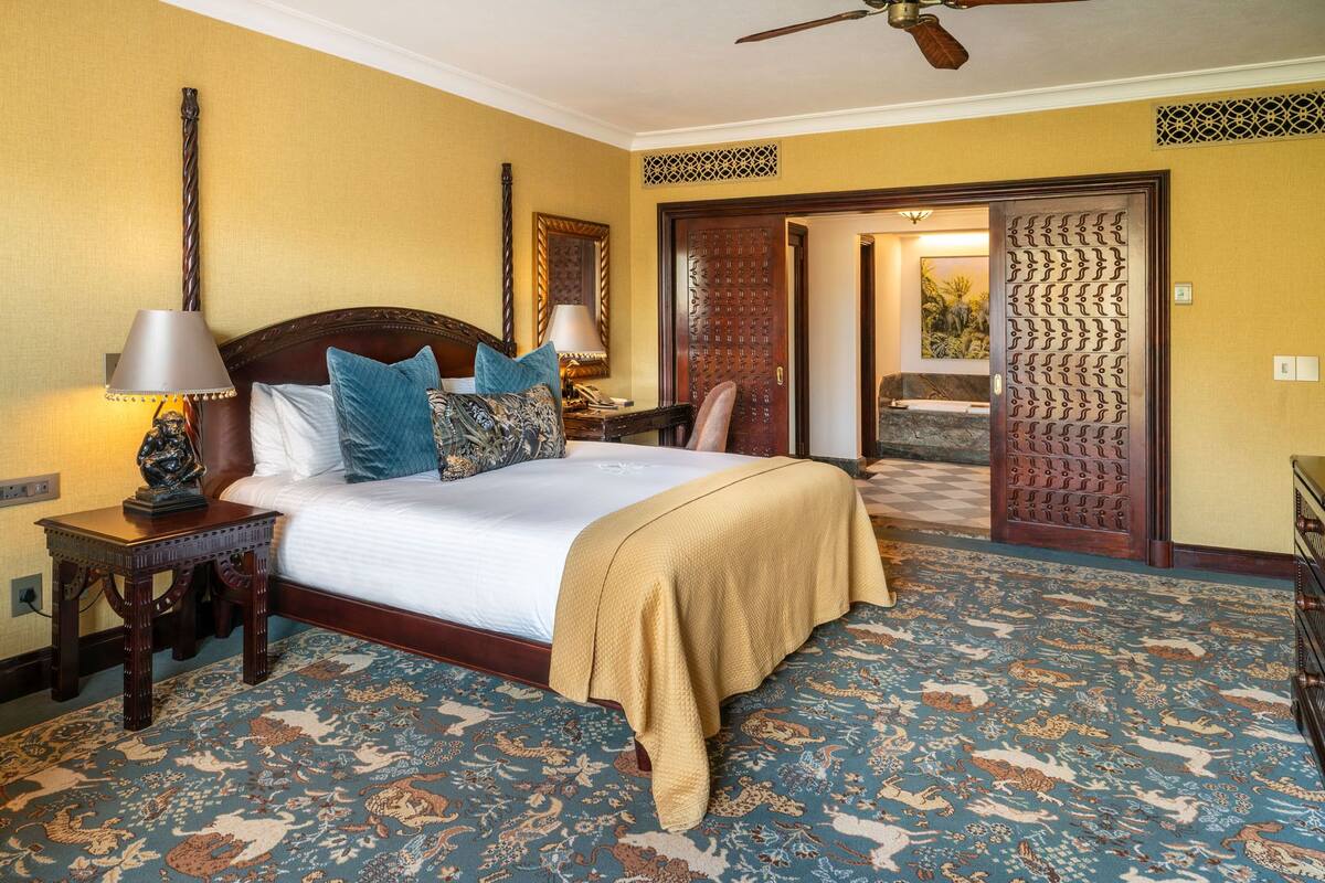A hotel room with a large bed, two bedside lamps, a wooden headboard, and a patterned carpet.