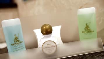 Drei Toilettenartikel auf einer Hotelzimmer-Ablagefläche: eine blaue Flasche mit dem Aufdruck 'Britannia Hotels Hair & Body Shampoo', eine klare Flasche mit goldfarbenem Verschluss, beschriftet mit 'The Collection', und eine grüne Flasche mit der Aufschrift 'Britannia Hotels Bath & Shower Gel'.