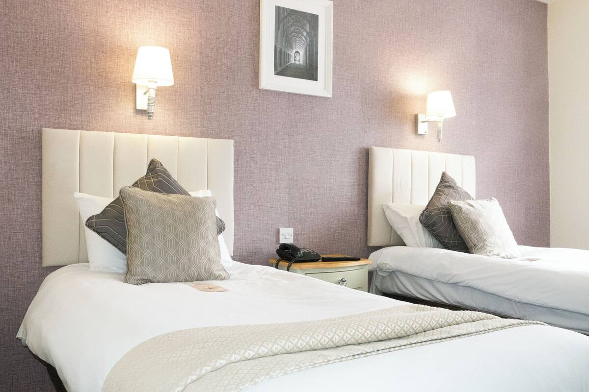 A hotel room with two beds, each with a headboard, a bedside table, and a lamp.