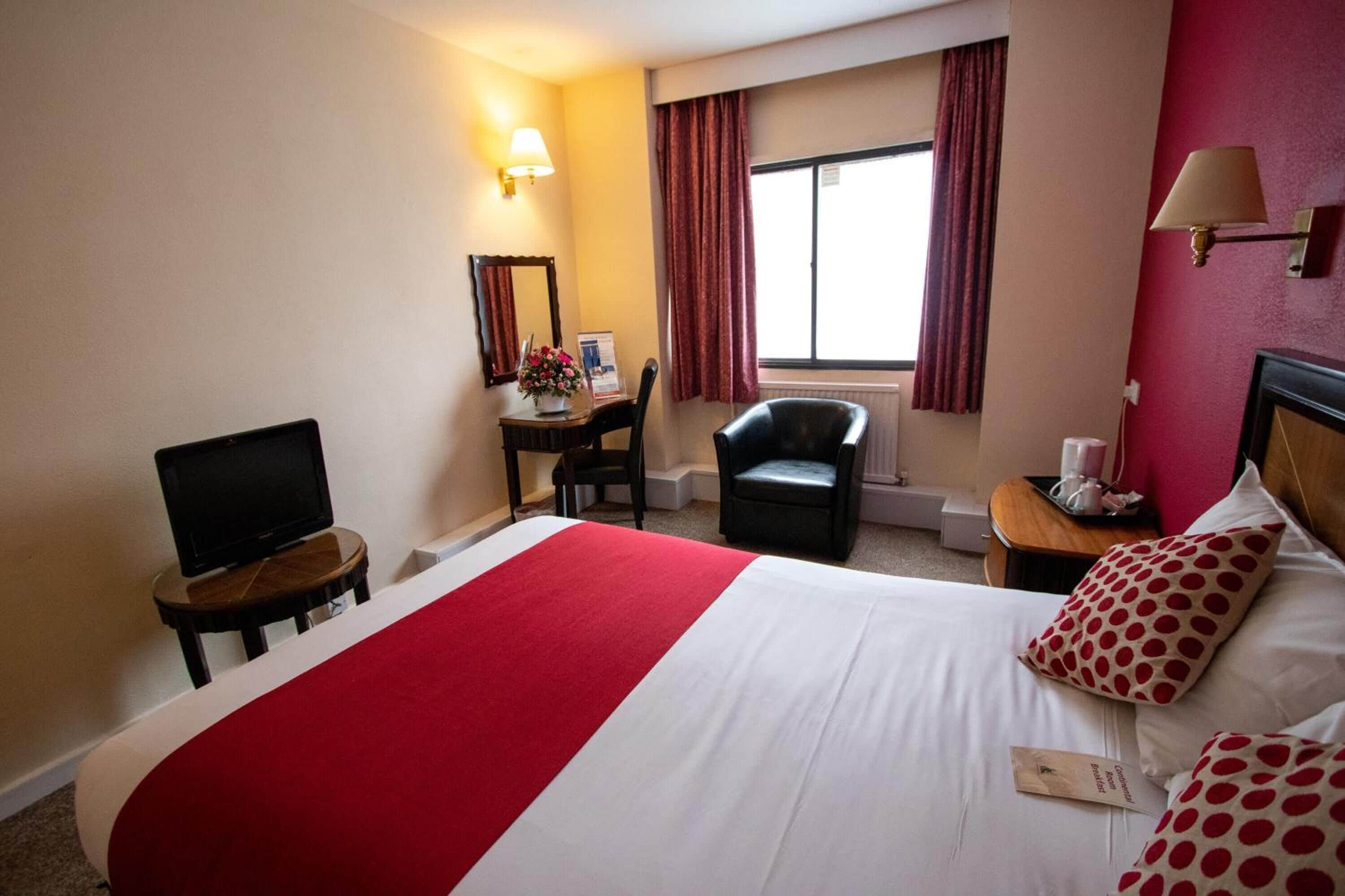 Una camera d'albergo con un letto grande, una scrivania con una sedia, una televisione e una finestra con tende.