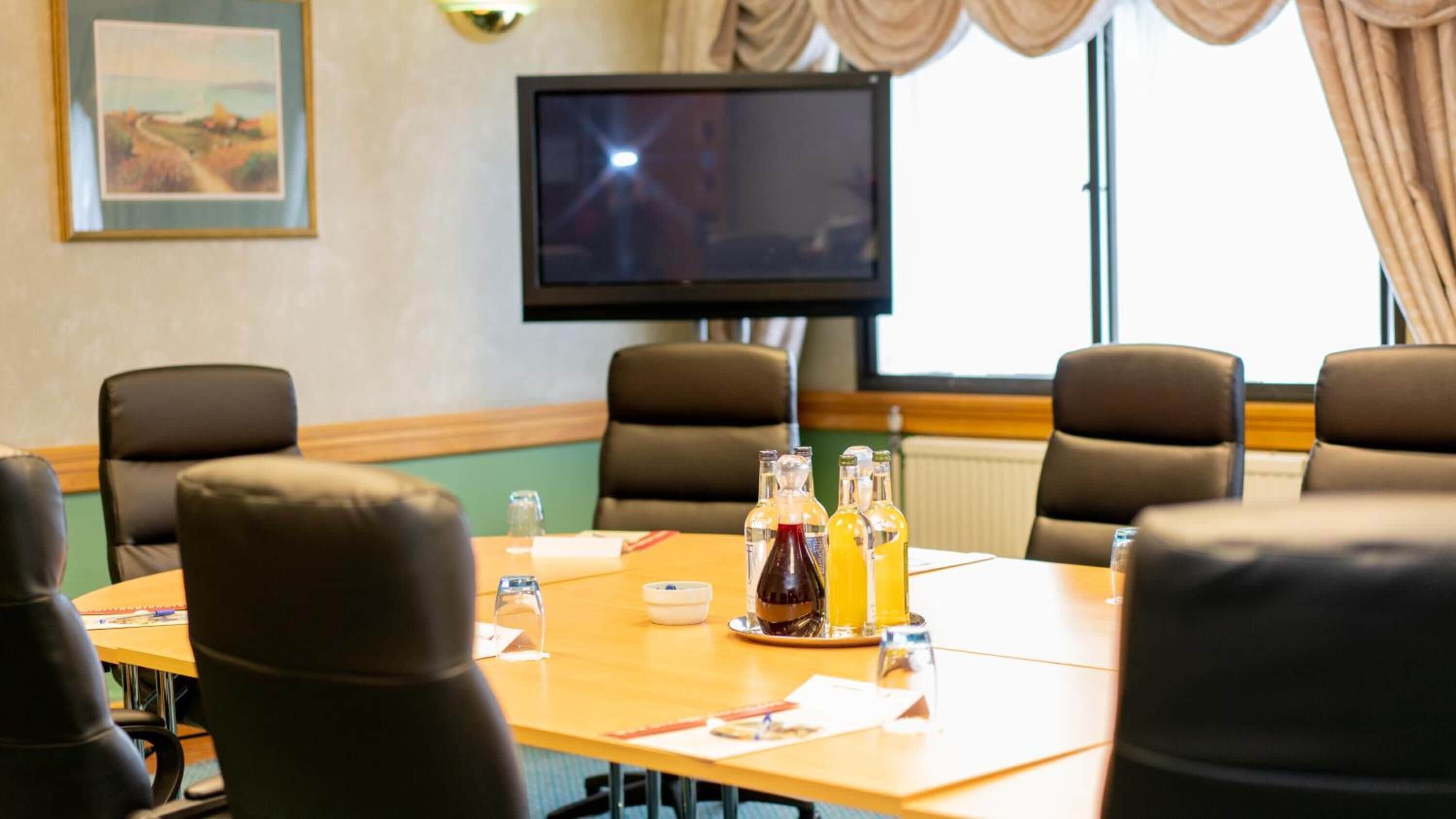 A conference room with a large table, chairs, a television, and various beverages.