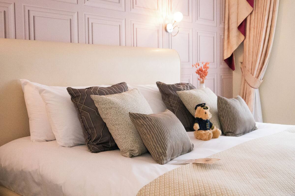 A neatly made bed with multiple pillows and a teddy bear.