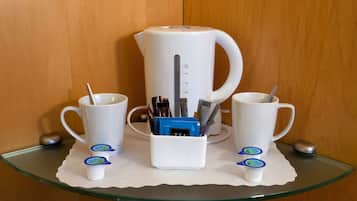 A coffee station with a white coffee maker, two white cups, and a white mug on a glass table.