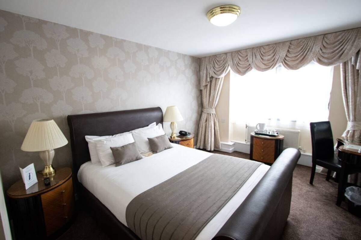 A hotel room with a large bed, two bedside tables with lamps, a chair, a desk, and a window with curtains.