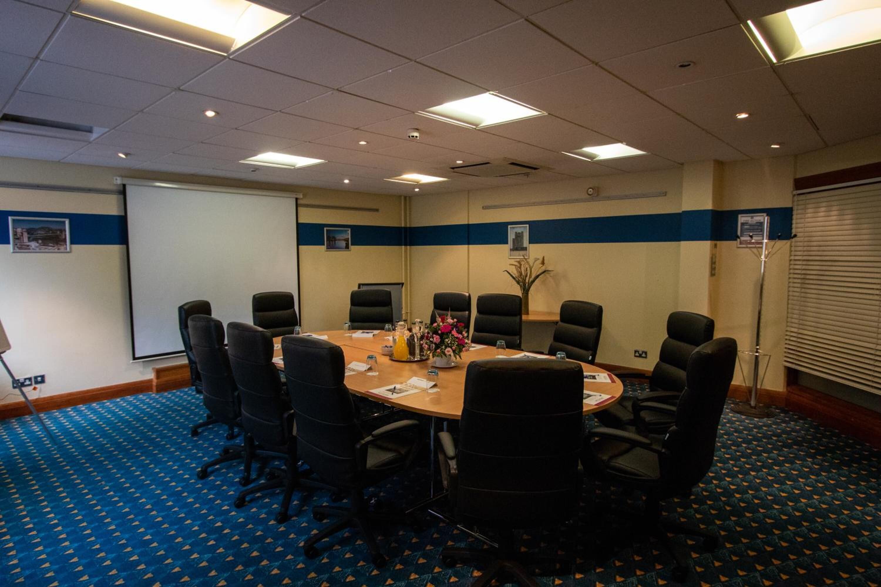 A conference room with a round table, black chairs, a projector screen, and a blue carpet.