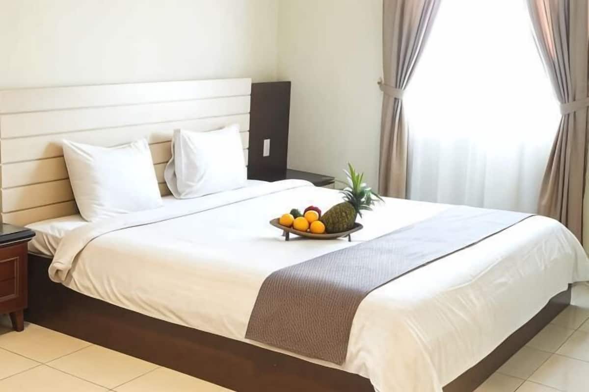 A neatly made bed with a fruit bowl, white bedding, and a nightstand.