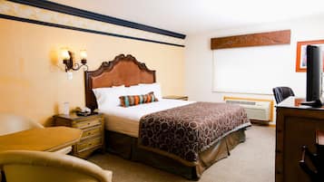 A hotel room with a large bed, bedside table, lamp, chair, desk, and a flat-screen TV.