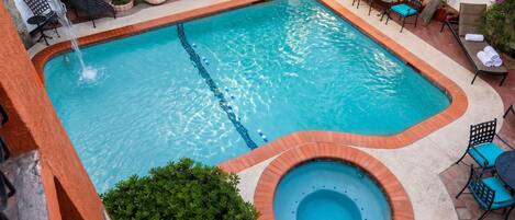 A rectangular swimming pool with a hot tub, surrounded by outdoor seating and potted plants.