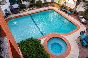 Una piscina rectangular con un jacuzzi, rodeada de mobiliario exterior y plantas en macetas.