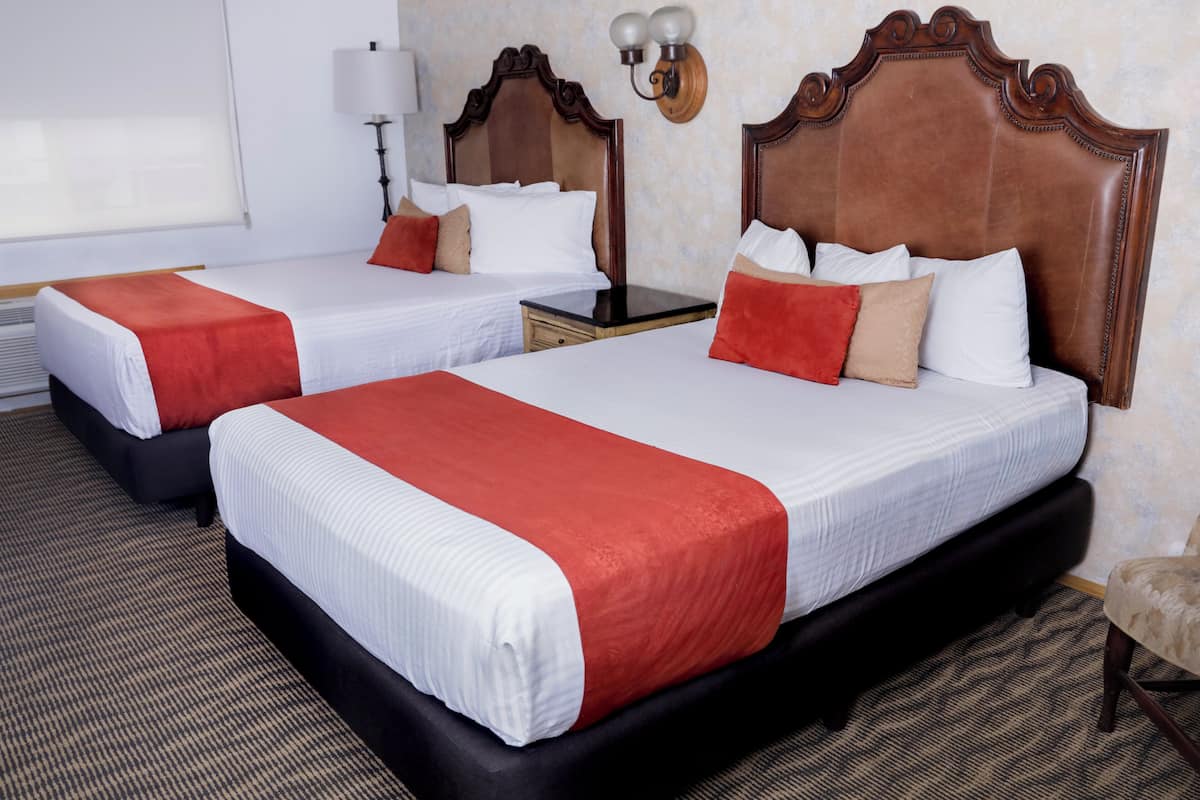 A hotel room with two beds, each with a red and white bedspread, a wooden headboard, a nightstand, a lamp, and a chair.
