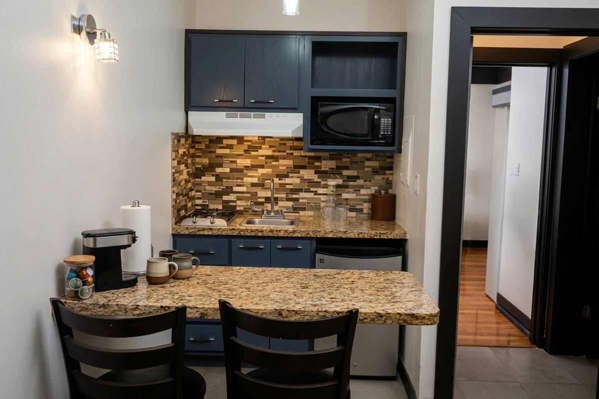 A compact kitchen with dark cabinets, a microwave, a granite countertop, and a tiled backsplash.